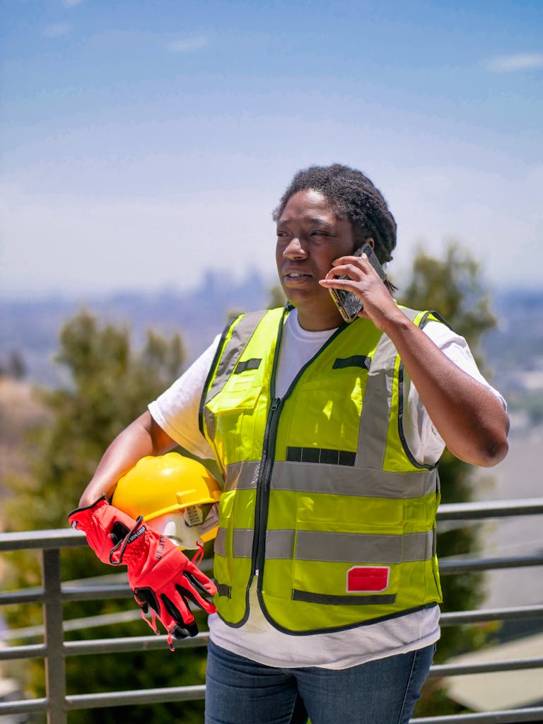 African American construction worker with safety gear using phone outdoors.